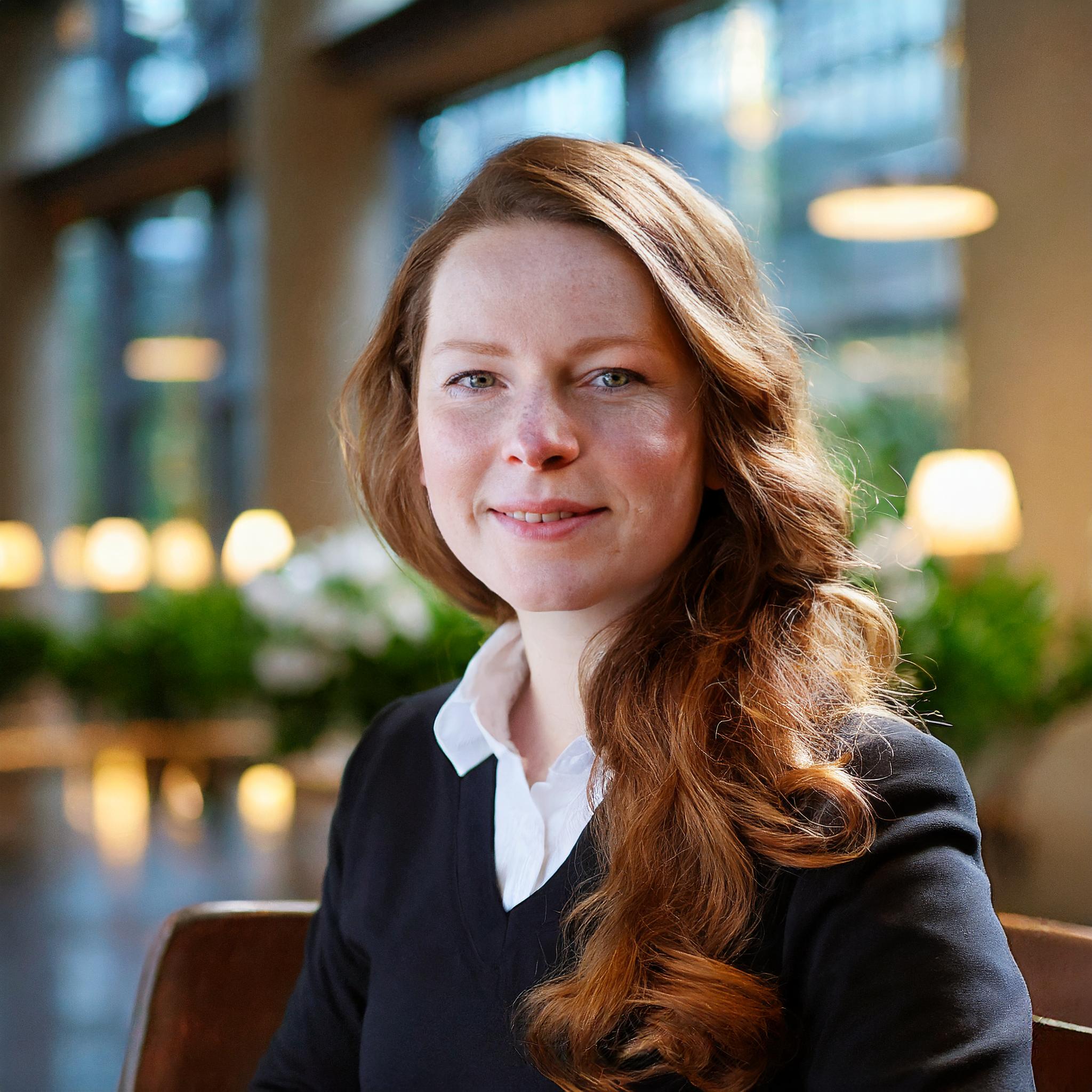 Porträt einer lächelnden Frau in den Dreißigern mit lockigem Haar.